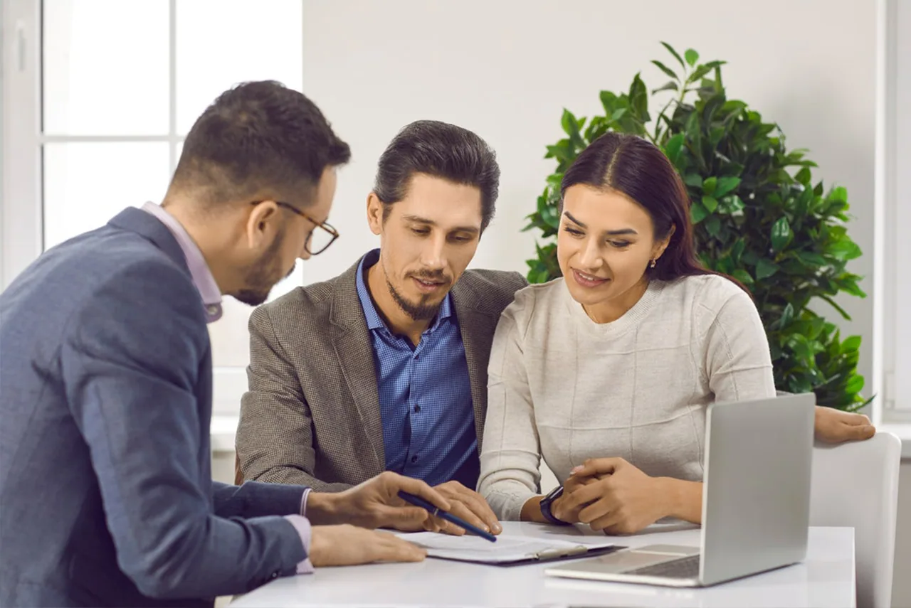 A couple and an advisor review documents together at a desk with a laptop.