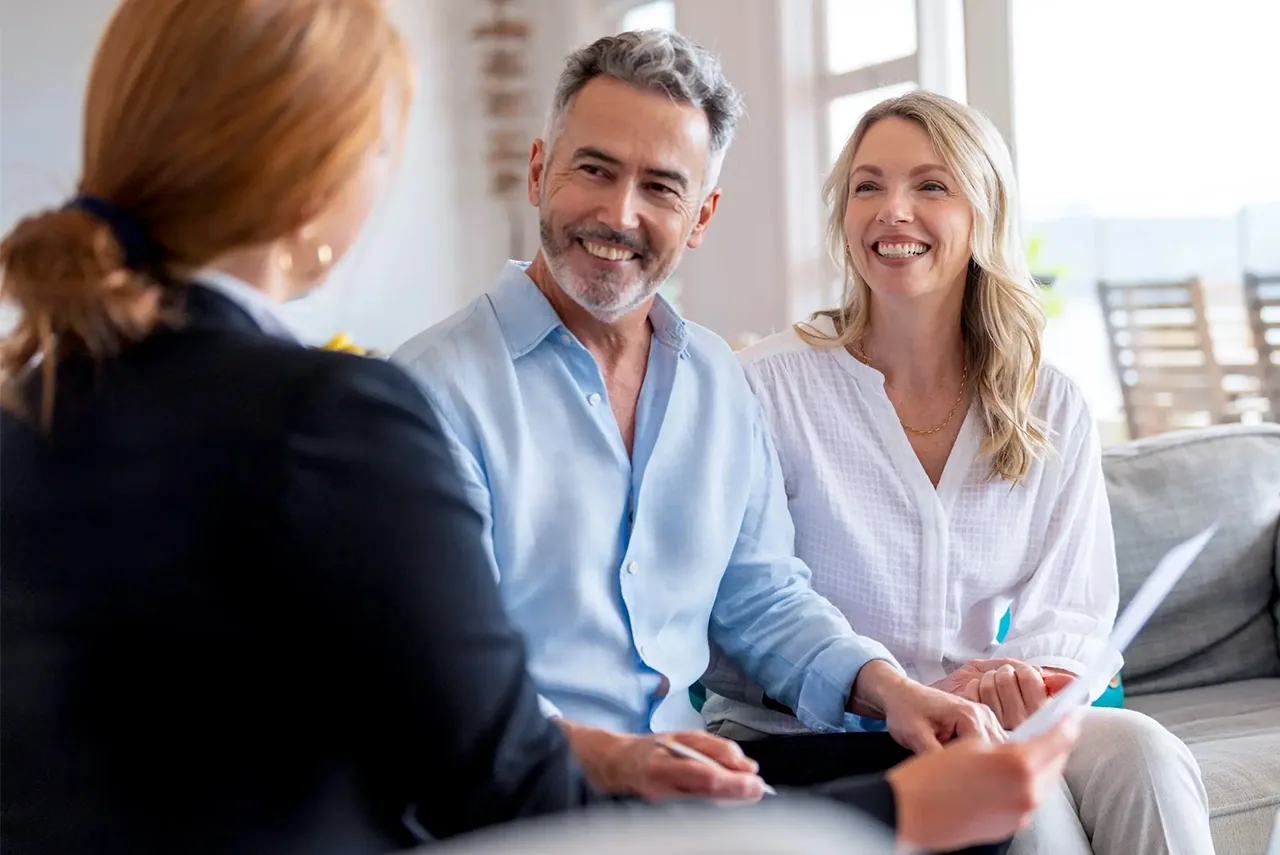 A smiling couple on a sofa reviews papers with an advisor.